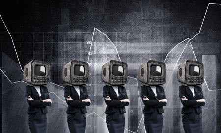 Business women in suits with old TV instead of their heads keeping arms crossed while standing against analytical charts drawn on wall on background.の写真素材