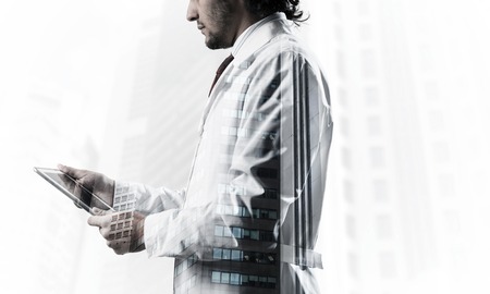 Double exposure of confident doctor in white sterile coat wirh modern cityscape view on background. Concept of modern medical industryの写真素材