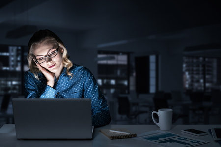 Young woman sitting in her room or office at late night. Mixed mediaの写真素材