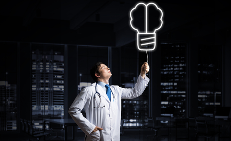 Professional medical industry employee in white medical suit interracting with glowing screw symbol in the air while standing against night cityscape view on background.の写真素材