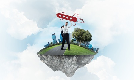Horizontal shot of successful and young businessman standing on the flying island and throwing huge rocket in the air with cloudy skyscape view on background.の写真素材