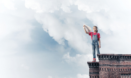 Cute happy kid girl on building top playing with paper planeの写真素材