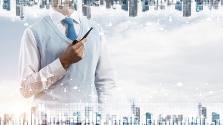Double exposure of confident and young businessman in smart-casual wear smoking pipe and modern cityscape with business and media interface. Concept networking for modern business.の写真素材
