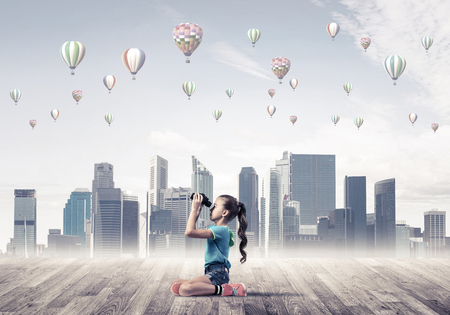 Cute kid girl sitting on wooden floor and aerostats flying in airの写真素材
