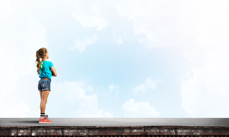 Cute kid girl standing on building roof with hands crossed on chestの写真素材