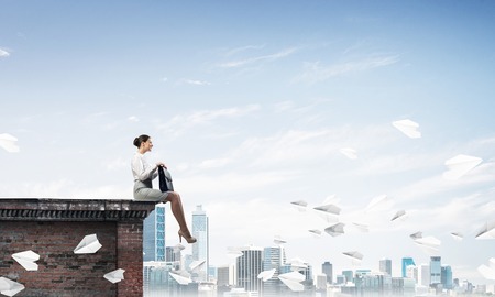 Young elegant woman with suitcase in hands siting on roof. Mixed mediaの写真素材