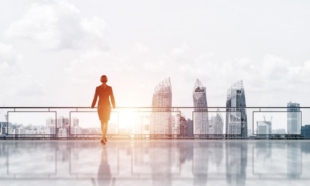 Young businesswoman in suit at balcony against morning cityscape backgroundの写真素材
