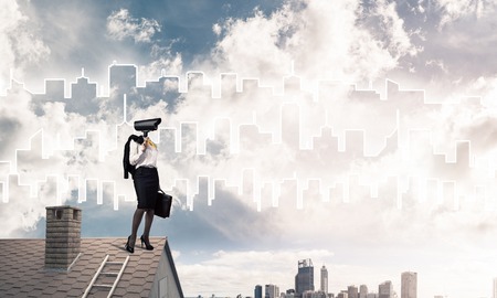 Faceless businesswoman with camera zoom instead of head standing on house roofの写真素材