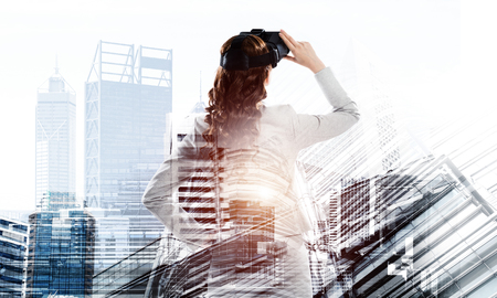 Double exposure of businesswoman wearing virtual reality glasses and modern cityscapeの写真素材