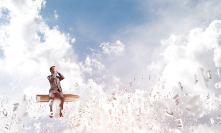 Young shocked businessman sitting on wooden book and covering eyes with palmsの写真素材