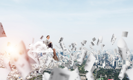 Young elegant woman with suitcase in hands siting on cloudの写真素材
