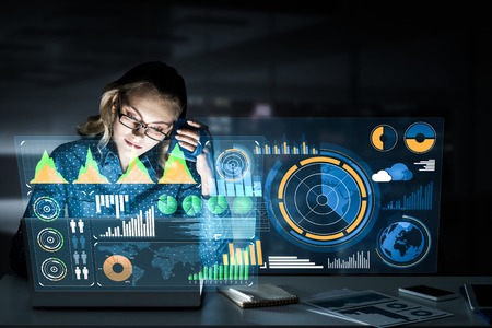 Attractive woman looking at her laptop screen sitting in night office. Mixed mediaの写真素材