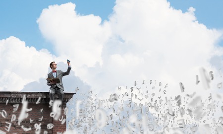 Funny man in red glasses and suit sitting on building top and reading bookの写真素材