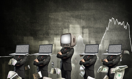 Businessmen in suits with laptops instead of their heads keeping arms crossed while standing in a row and one at the head with old TV against analytical charts on background.の写真素材