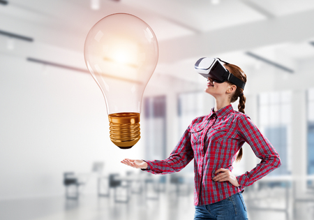 Young woman in virtual reality helmet and glass light bulb. Mixed mediaの写真素材