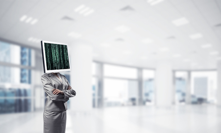 Cropped image of business woman in suit with monitor instead of head keeping arms crossed while standing inside office building.の写真素材