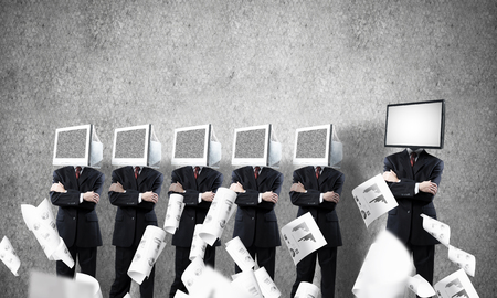 Businessmen in suits with monitors instead of their heads keeping arms crossed while standing in a row and one at the head with TV in empty room against gray wall on background.の写真素材