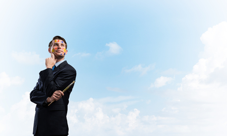 Portrait of young thoughtful man holding paintbrush in his hand and looking away while standing against blue cloudy skyscape on background.の写真素材