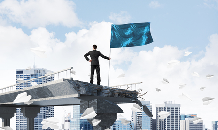 Rear view of confident businessman in suit holding flag in hand while standing among flying paper planes on broken bridge with cityscape on background. 3D rendering.の写真素材