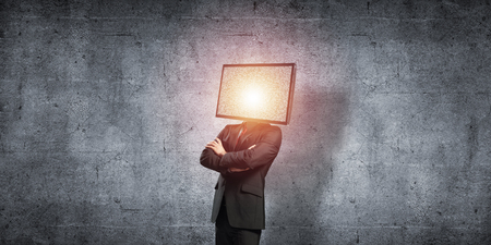 Businessman in suit with TV instead of head keeping arms crossed while standing against gray dark wall on background.の写真素材