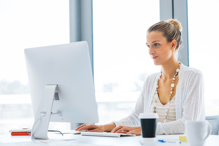 Attractive young woman sitting at desk and working on her computerの写真素材