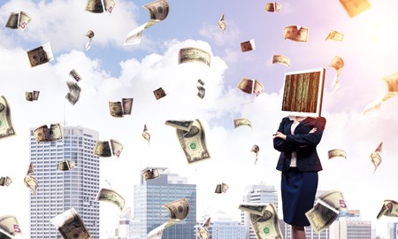 Cropped image of business woman in suit with monitor instead of head keeping arms crossed while standing outdoors among flying dollars with cityscape view on background.の写真素材