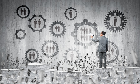 Businessman with speaker in hand standing among flying letters with social gear structure on background. Mixed media.の写真素材
