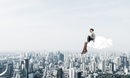 Young elegant woman with suitcase in hands siting on cloudの写真素材