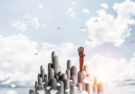 Businessman in suit with an old TV instead of head keeping arms crossed while standing on the top of stone columns among flying paper planes with beautiful landscape on background. 3D rendering.の写真素材