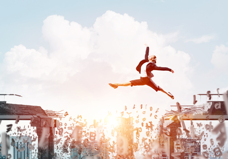 Business woman jumping over gap with flying letters in concrete bridge as symbol of overcoming challenges. Cityscape with sunlight on background. 3D rendering.の写真素材
