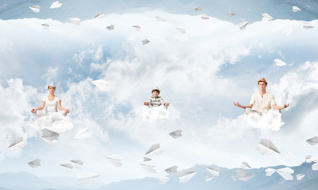 Young family keeping eyes closed and looking concentrated while meditating on clouds among flying paper planes and between two nature worlds.の写真素材