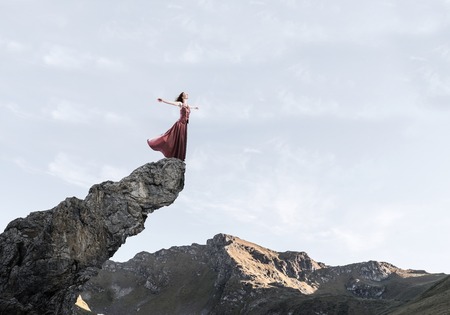 Young attractive woman relaxing in summer day standing on rock topの写真素材