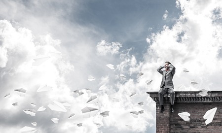 Frustrated businessman sitting on roof and closing ears with handsの写真素材