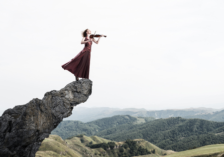 Young attractive girl playing violin standing at top of rockの写真素材