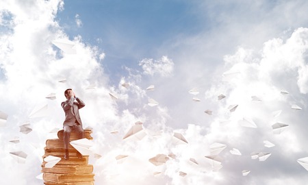 Young shocked businessman sitting on old book and covering eyes with palmsの写真素材