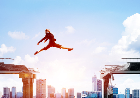 Business woman jumping over gap in concrete bridge as symbol of overcoming challenges. Cityscape with sunlight on background. 3D rendering.の写真素材