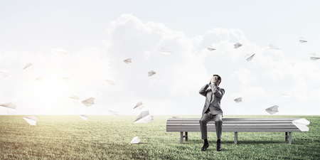 Young shocked businessman sitting on wooden bench and covering eyes with palmsの写真素材