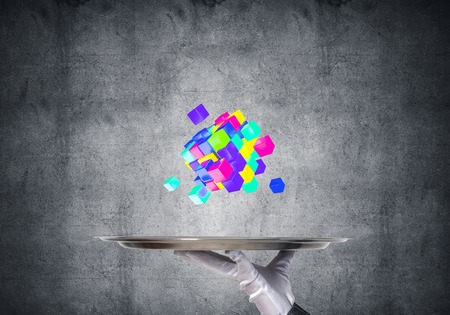 Cropped image of waitresss hand in white glove presenting multiple cubes on metal tray with gray wall on background. 3D rendering.の写真素材
