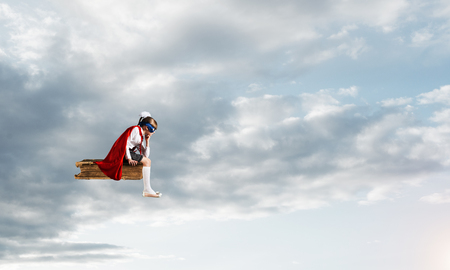 Little sad child in mask and cape floating on book in skyの写真素材