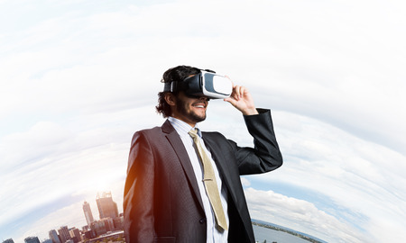 Young handsome businessman in virtual helmet against cityscape background