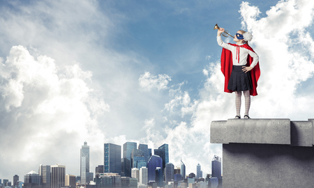 Young girl in superhero costume standing on building roof. Mixed mediaの写真素材