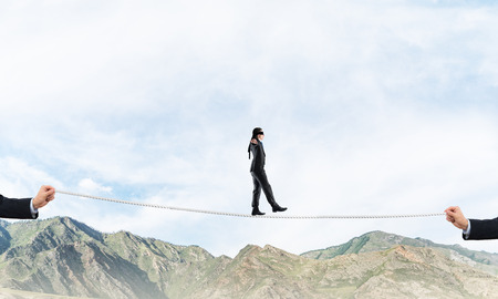 Businessman walking blindfolded on rope above high mountains as symbol of hidden threats and support. Skyscape and nature view on background.の写真素材