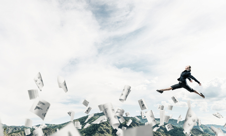 Attractive business woman in suit jumping in the air among flying papers as symbol of active life position. Skyscape and nature view on background. 3D rendering.の写真素材