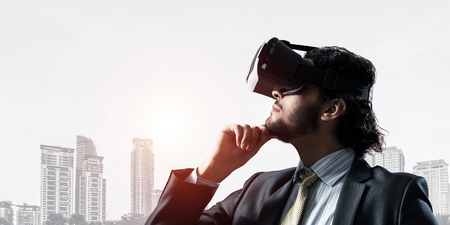 Young handsome businessman in virtual helmet against cityscape background