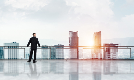 Young businessman in suit at balcony against morning cityscape backgroundの写真素材
