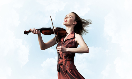 Young attractive girl playing violin over blue sky and cloudの写真素材