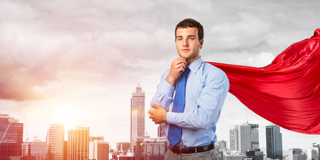 Young pensive businessman wearing red cape against modern city backgroundの写真素材