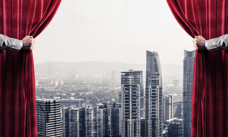 Hands of businessman opening red velvet curtain and cityscape at backgroundの写真素材