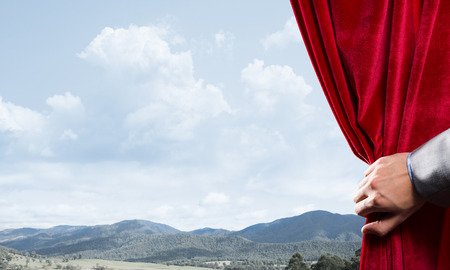 Human hand opens red curtain on natural landscape backgroundの写真素材