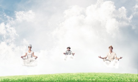 Young family keeping eyes closed and looking concentrated while meditating on clouds in the air with bright and beautiful landscape on background.の写真素材